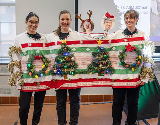 three people dressed in a single sweater adorned with holiday decorations